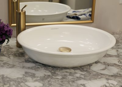 Bathroom vessel sink with brass faucet, framed mirror, marble counter, and floral accent