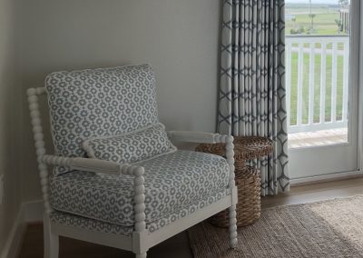 Beach house bedroom accent chair with blue patterned cushion, woven side table, and balcony view