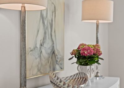 Bedroom nightstand with table lamp, floral arrangement, decorative bowl, and wall art