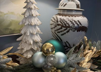 Blue and gold holiday console styling with ornaments, greenery, metallic leaves, and white Christmas tree accents