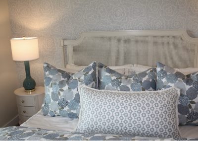 Blue and neutral bedroom interior design with layered pillows, textured wallpaper, and designer bedside lighting