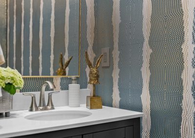 Powder bathroom with blue patterned wallpaper, framed mirror, and dark vanity
