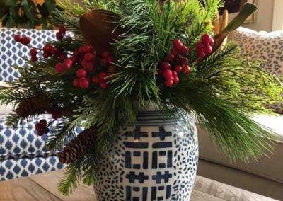 Christmas greenery floral centerpiece with red berries, roses, pine branches, and a blue and white vase