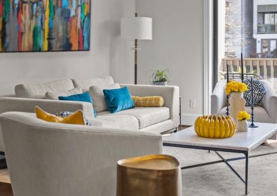 Bright living room with abstract art, white sofa, blue pillows, and yellow accents