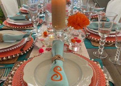 Colorful summer tablescape with coral chargers, turquoise linens, and candle centerpiece