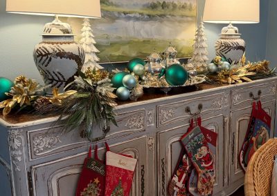 Elegant Christmas console with stockings, blue and gold ornaments, lamps, garland, and white tree decor