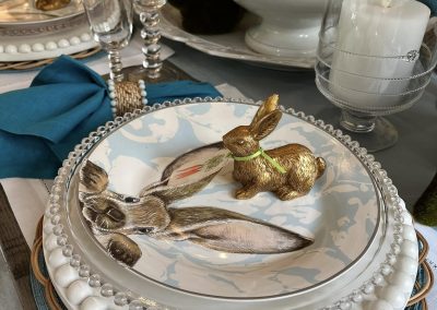 Elegant holiday place setting with layered plates, blue napkin, crystal glassware, candles, and floral centerpiece