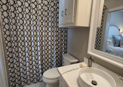 Guest bathroom with patterned shower curtain, marble vanity, vessel sink, and framed mirror