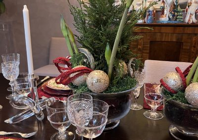 Holiday tablescape with evergreen centerpiece, red linens, crystal stemware, candles, and ornament accents