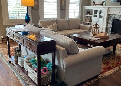 Living room before redesign with neutral sofas, dark tables, built-ins, and patterned rug