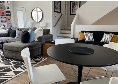 Modern living room with black round dining table, gray sofa, staircase, and graphic rug