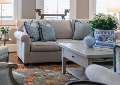 Neutral living room with blue pillows, white coffee table, floral arrangement, and sofa seating