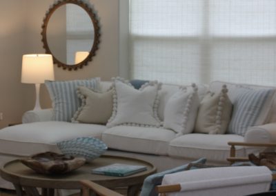 Neutral sitting room with layered pillows, round coffee table, mirrors, and table lamp