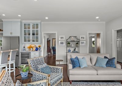 Open-concept living room and kitchen with blue accents, patterned chairs, and bright windows