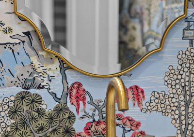 Powder bathroom with floral wallpaper, brass faucet, scalloped mirror, and marble counter