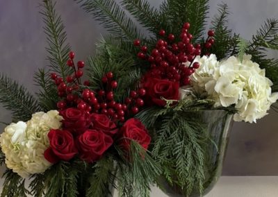 Red and white Christmas floral arrangement with roses, hydrangeas, evergreen branches, and berries