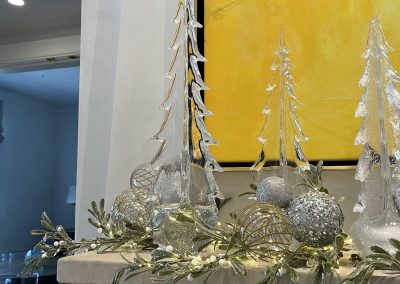 Silver and white Christmas mantel with glass trees, ornaments, greenery, and modern holiday decor