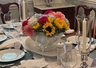 Spring entertaining table with sunflower floral centerpiece, blue placemats, and crystal candleholders