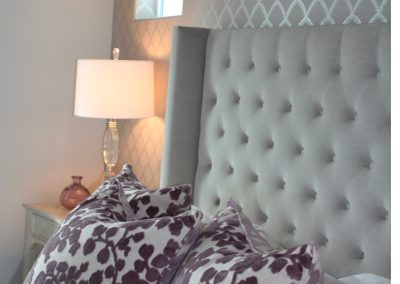 Bedroom detail with tufted headboard, patterned bedding, wall sconces, and soft blue tones