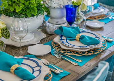 Turquoise coastal-inspired tablescape with woven chargers, blue linens, and greenery centerpiece
