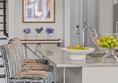 White kitchen breakfast bar with striped stools, pendant lights, and fresh green accents