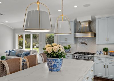 White kitchen island with floral arrangement, pendant lights, range hood, and bar seating