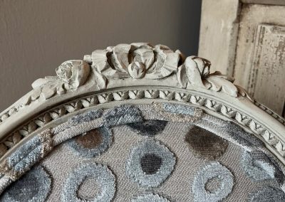 Close-up of refreshed armchair with gray circular upholstery and carved painted frame