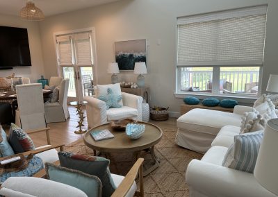 Coastal open-concept living room with white seating, woven textures, blue accents, and balcony views