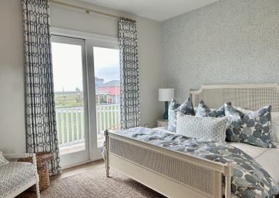 Coastal primary bedroom with cane bed, blue patterned bedding, custom curtains, and balcony doors