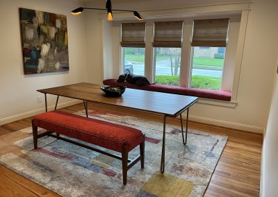 Modern dining room with wood table, red bench seating, abstract art, window seat, and woven shades
