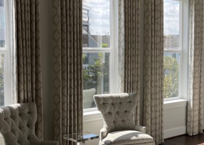 Three windows after custom drapery with patterned panels, upholstered chairs, and acrylic table