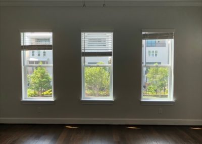 Three windows before custom drapery with simple shades and dark wood floors