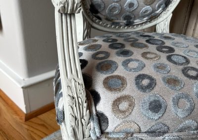 Detail of carved armchair frame with distressed finish and gray patterned fabric