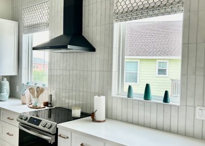 White kitchen with black range hood, vertical tile backsplash, and patterned Roman shades