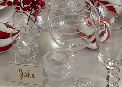 Close-up of a Christmas tablescape featuring crystal glassware, red berry accents, peppermint ornaments, glass trees, and elegant place settings.