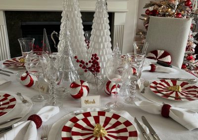 Elegant peppermint Christmas tablescape with red and white striped plates, crystal glassware, glass Christmas trees, and festive berry accents.
